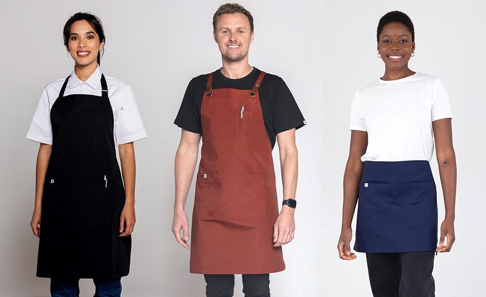 Arlo, Luca Bib, and Luca Waist Aprons Three staff members wearing different apron styles: Arlo full-length bib apron in black, Luca bib apron in rust with brown leather straps, and Luca waist apron in navy